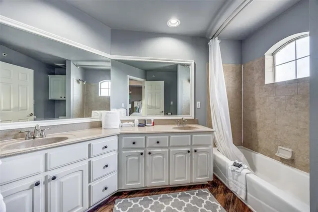 a bathroom with a double vanity sink a mirror a bathtub and next to a window