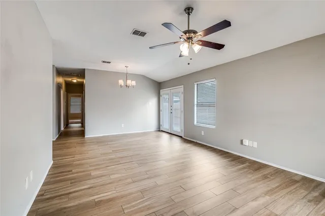 a view of an empty room with wooden floor and a ceiling fan