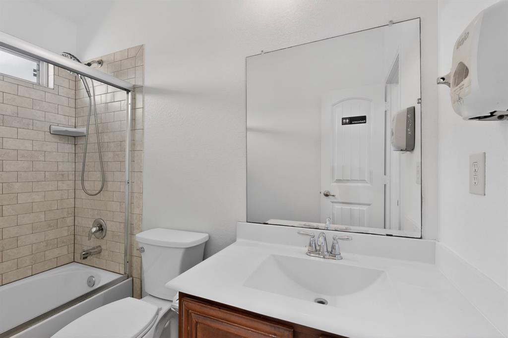 426 Harding Lane Lavon, TX 75166 - Photo 37 of 40 Bathroom featuring a ceramic tile shower surround, shower/tub combination with sliding glass door, white vanity countertop with integrated sink, and wood-finish vanity cabinetry