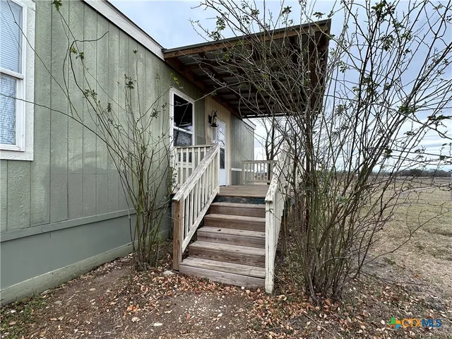 a view of a pathway of a house with wooden fence and large trees