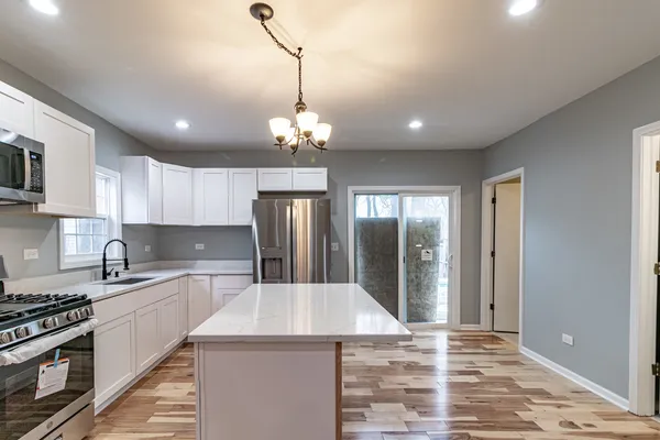 a kitchen with stainless steel appliances kitchen island a sink dishwasher a stove and a refrigerator with wooden floor