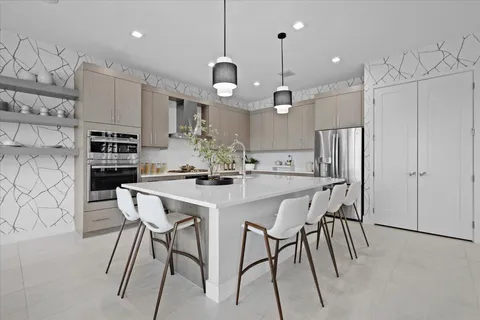 a kitchen with stainless steel appliances kitchen island granite countertop a dining table chairs and a refrigerator