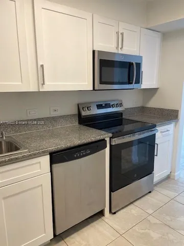 a kitchen with stainless steel appliances granite countertop white cabinets and a stove top oven