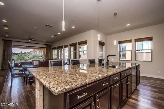 a kitchen with stainless steel appliances kitchen island granite countertop a stove top oven a sink dishwasher a dining table and chairs with wooden floor