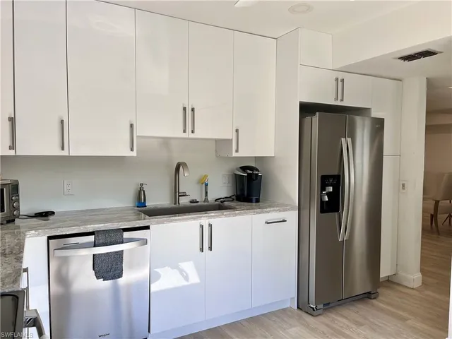 a kitchen with stainless steel appliances granite countertop a refrigerator a sink and white cabinets