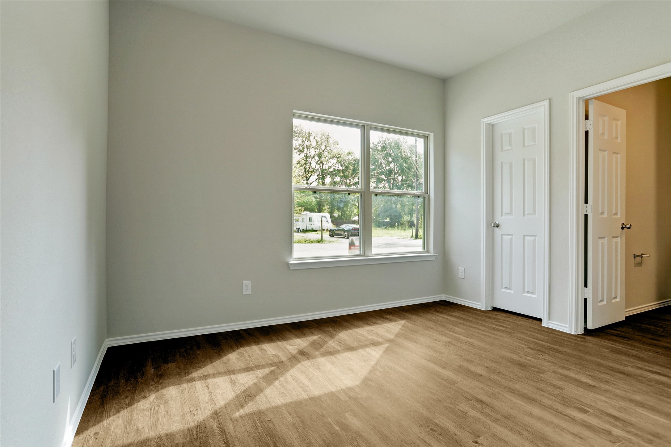 409 South 12th Street, Unit B Conroe, TX 77301 - Photo 10 of 14 Bright room with large window, wood flooring, and neutral walls. Features a closet and an additional door, offering a cozy space with a view of greenery outside.