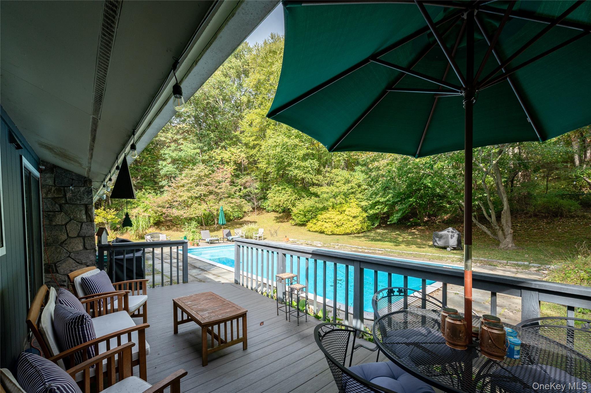 29 Alice Road Mount Kisco, NY 10549 - Photo 23 of 24 Deck with an outdoor pool, outdoor dining area, and view of wooded backyard