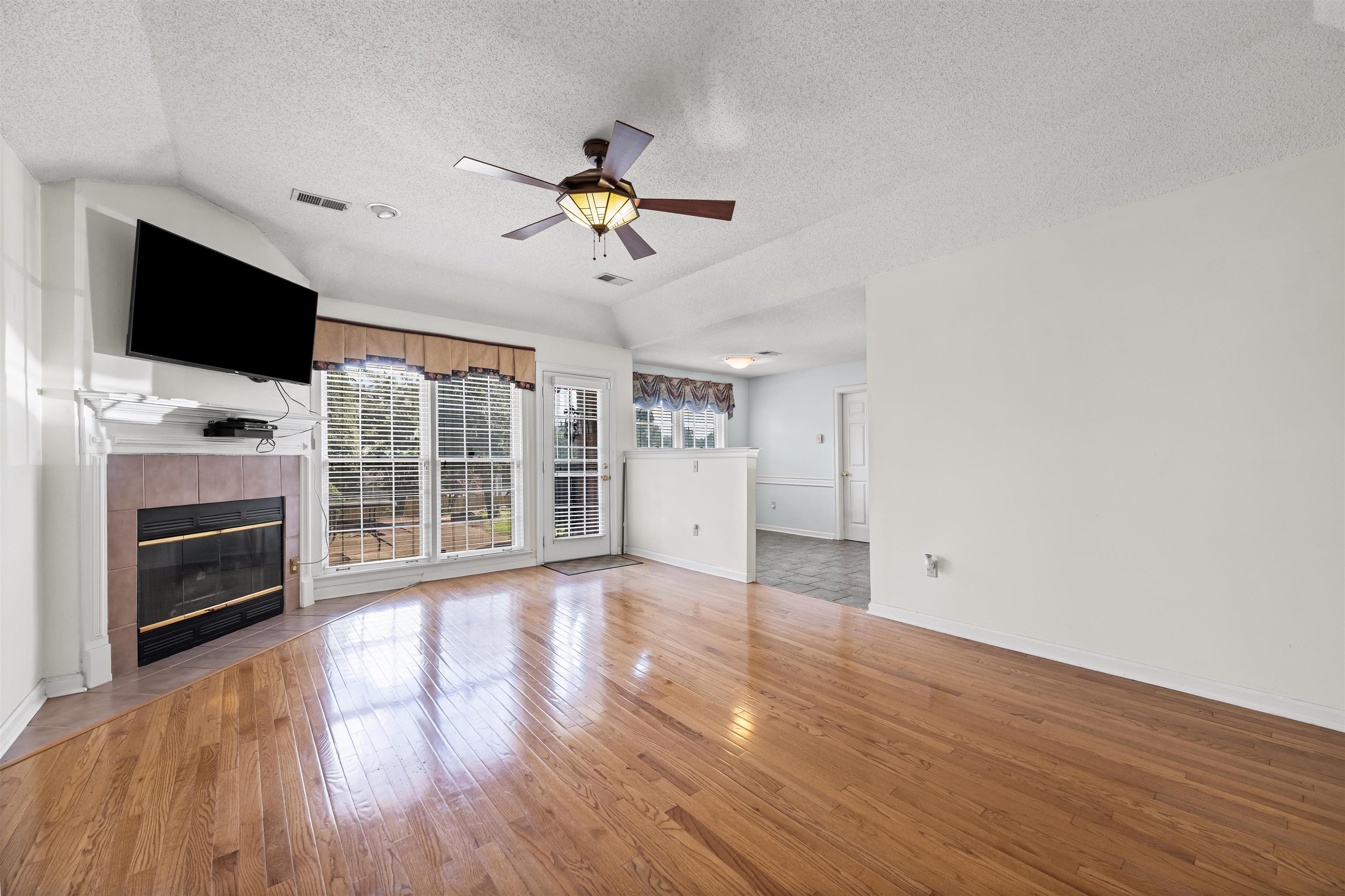 8645 Bazemore Road Memphis, TN 38018 - Photo 13 of 28 Unfurnished living room with a textured ceiling, vaulted ceiling, ceiling fan, light wood-type flooring, and a tile fireplace