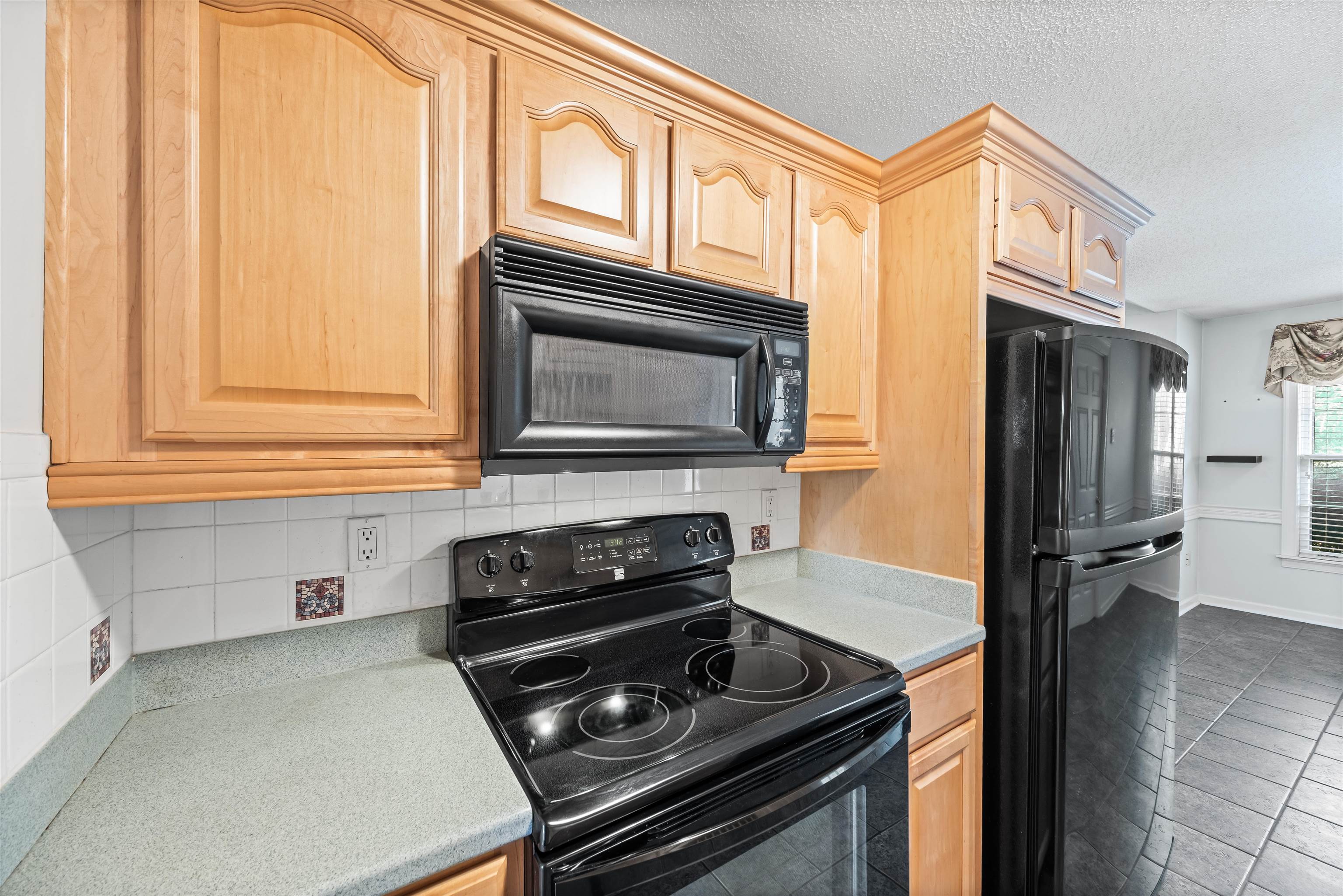 8645 Bazemore Road Memphis, TN 38018 - Photo 9 of 28 Kitchen featuring black appliances, decorative backsplash, light brown cabinets, and a textured ceiling