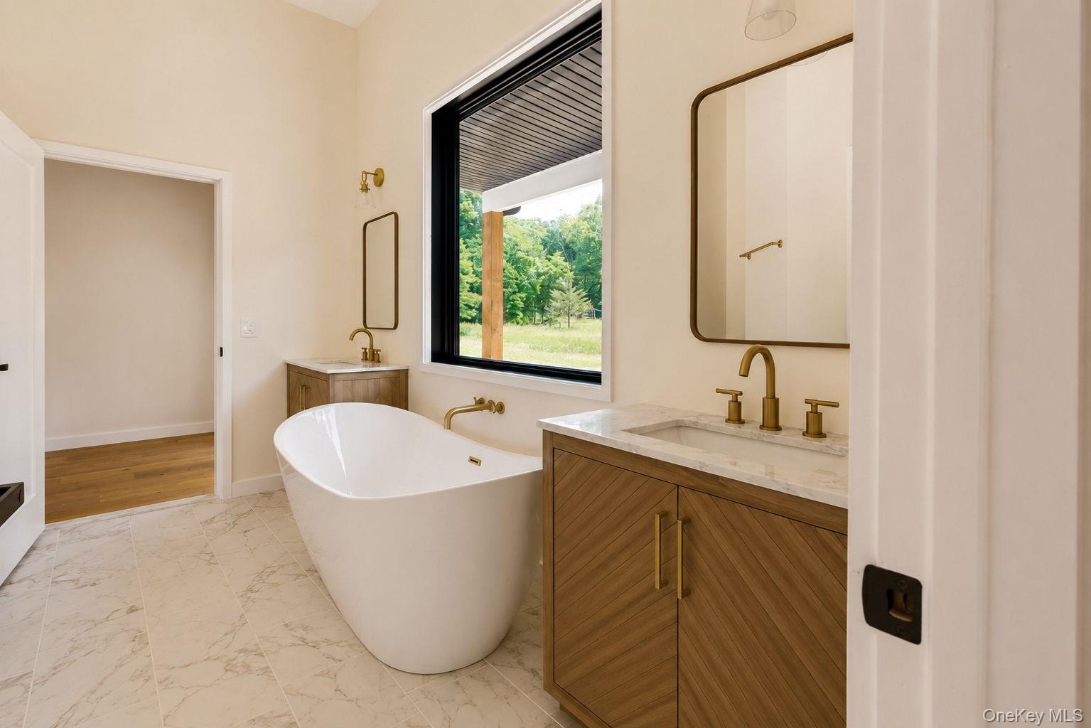 128 St Elmo Road Wallkill, NY 12589 - Photo 19 of 45 Bathroom featuring a freestanding soaking tub, dual wood-finish vanities with rectangular sinks and light-colored countertops, and gold-finish fixtures