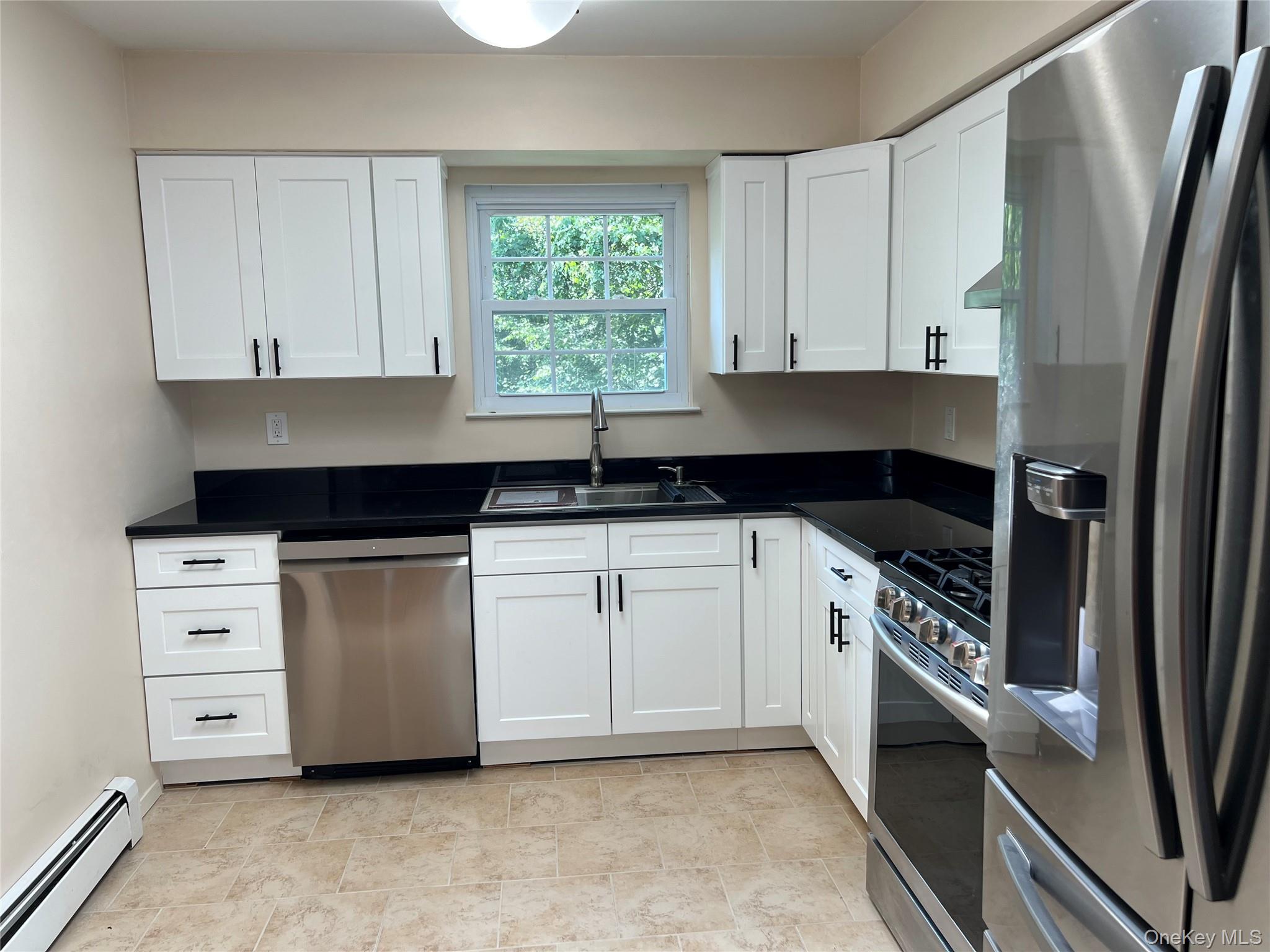 Kitchen with stainless steel appliances, baseboard heating, white cabinets, and granite countertops
