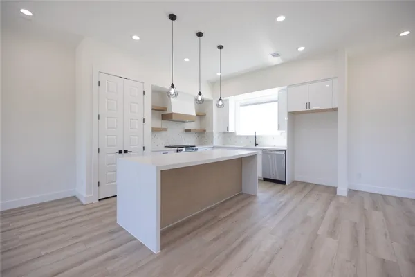 a large kitchen with stainless steel appliances a large counter top a sink a refrigerator and a window