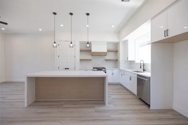a large kitchen with stainless steel appliances a large counter top a stove a sink dishwasher a refrigerator and white cabinets with wooden floor