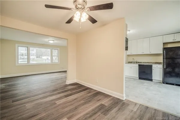 an empty room with wooden floor a ceiling fan and kitchen view
