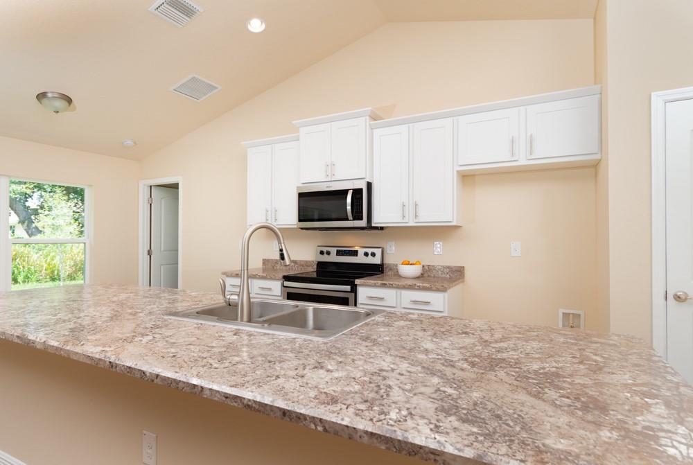 1391 Seahouse Street Sebastian, FL 32958 - Photo 9 of 18 a kitchen with granite countertop a stove a sink and a microwave