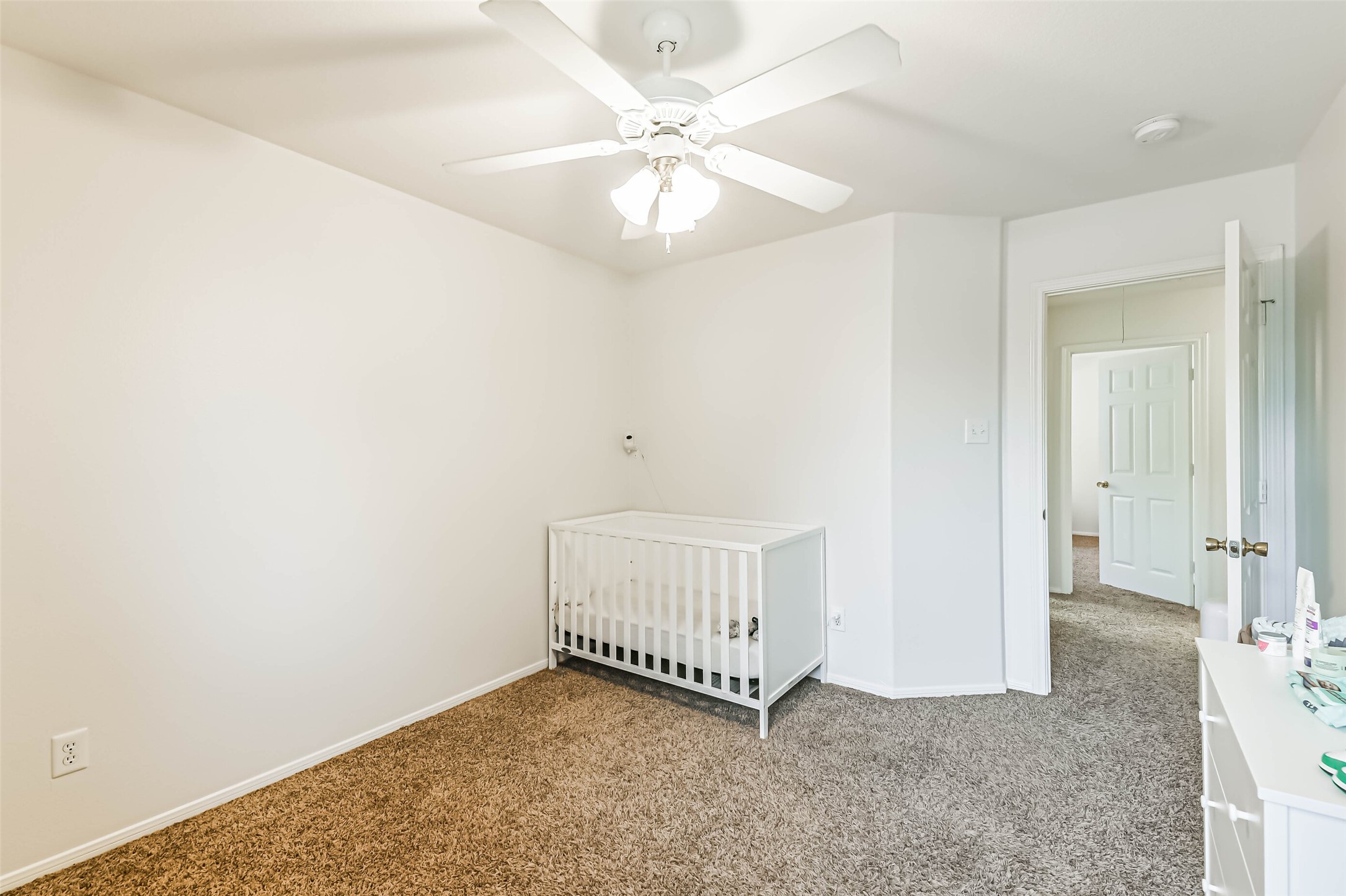 22538 Goss Spring Court Spring, TX 77373 - Photo 29 of 36 This is a cozy, carpeted bedroom featuring a ceiling fan, white walls, and a crib, ideal for a nursery or child's room. It connects to a hallway through an open door.