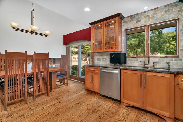 a kitchen with stainless steel appliances granite countertop a refrigerator a sink dishwasher a stove and a dining table with wooden floor