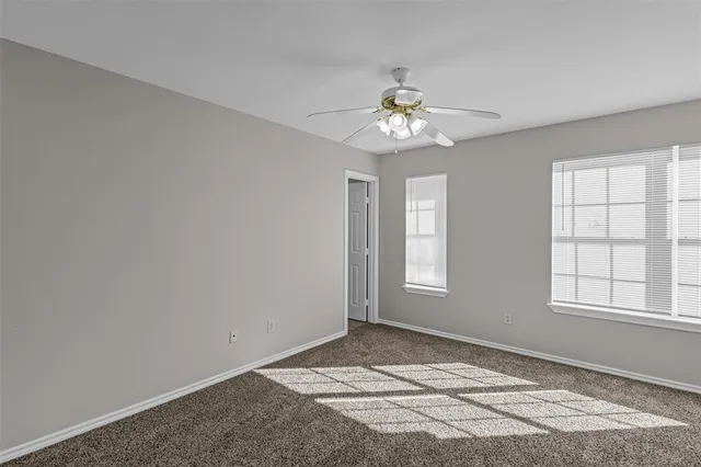 an empty room with chandelier fan and windows