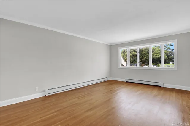a view of an empty room with wooden floor and windows