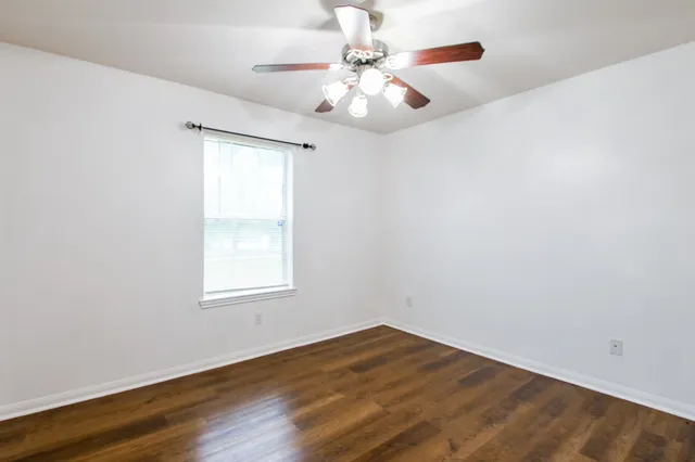 an empty room with wooden floor chandelier fan and windows