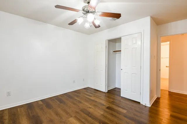 an empty room with wooden floor chandelier fan and windows