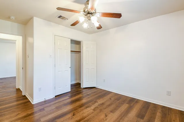 an empty room with wooden floor fan and windows