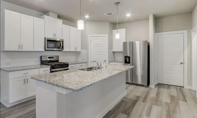 a kitchen with stainless steel appliances granite countertop a refrigerator a sink a stove a microwave and white cabinets with wooden floor