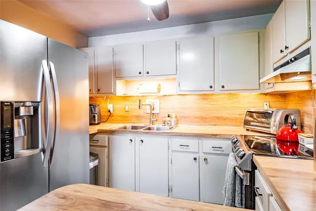 a kitchen with stainless steel appliances granite countertop a refrigerator a sink a stove and white cabinets