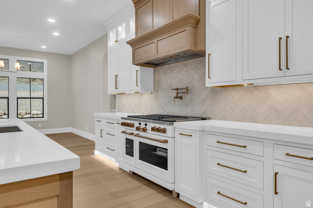 2828 Jojo Road Eagle Mountain, UT 84005 - Photo 14 of 63 Gourmet kitchen featuring a large professional-grade range, white perimeter cabinetry with brass-toned hardware, light wood-finish flooring, and a herringbone pattern tile backsplash