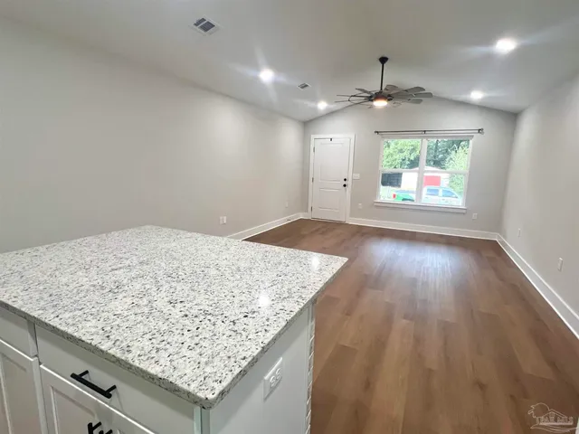 an empty room with wooden floor and kitchen view