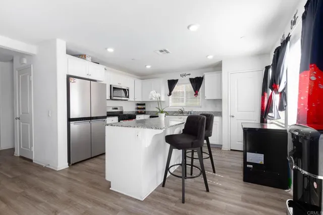 a kitchen with stainless steel appliances granite countertop a refrigerator a stove top oven a sink dishwasher and white cabinets with wooden floor