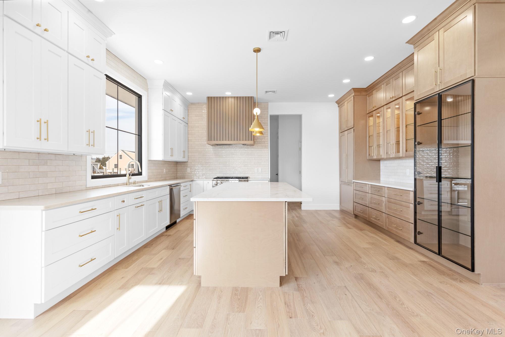 24 Midway Street Babylon, NY 11702 - Photo 12 of 40 Kitchen with a center island, hanging light fixtures, light stone counters, light wood-type flooring, and glass insert cabinets