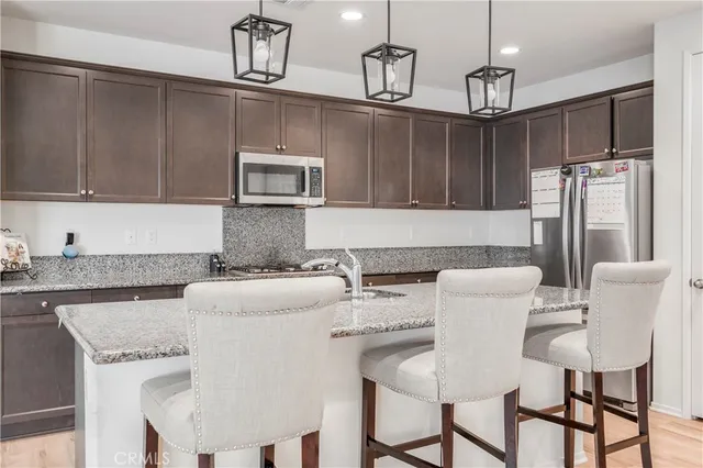 a kitchen with stainless steel appliances granite countertop a dining table chairs refrigerator and microwave