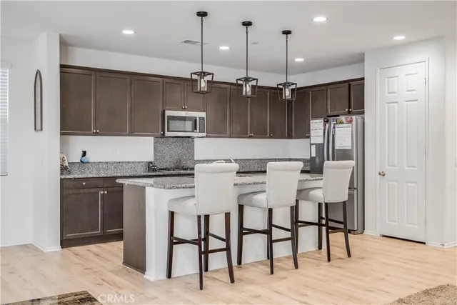 a kitchen with stainless steel appliances kitchen island granite countertop a refrigerator a stove a sink and a oven with wooden floor