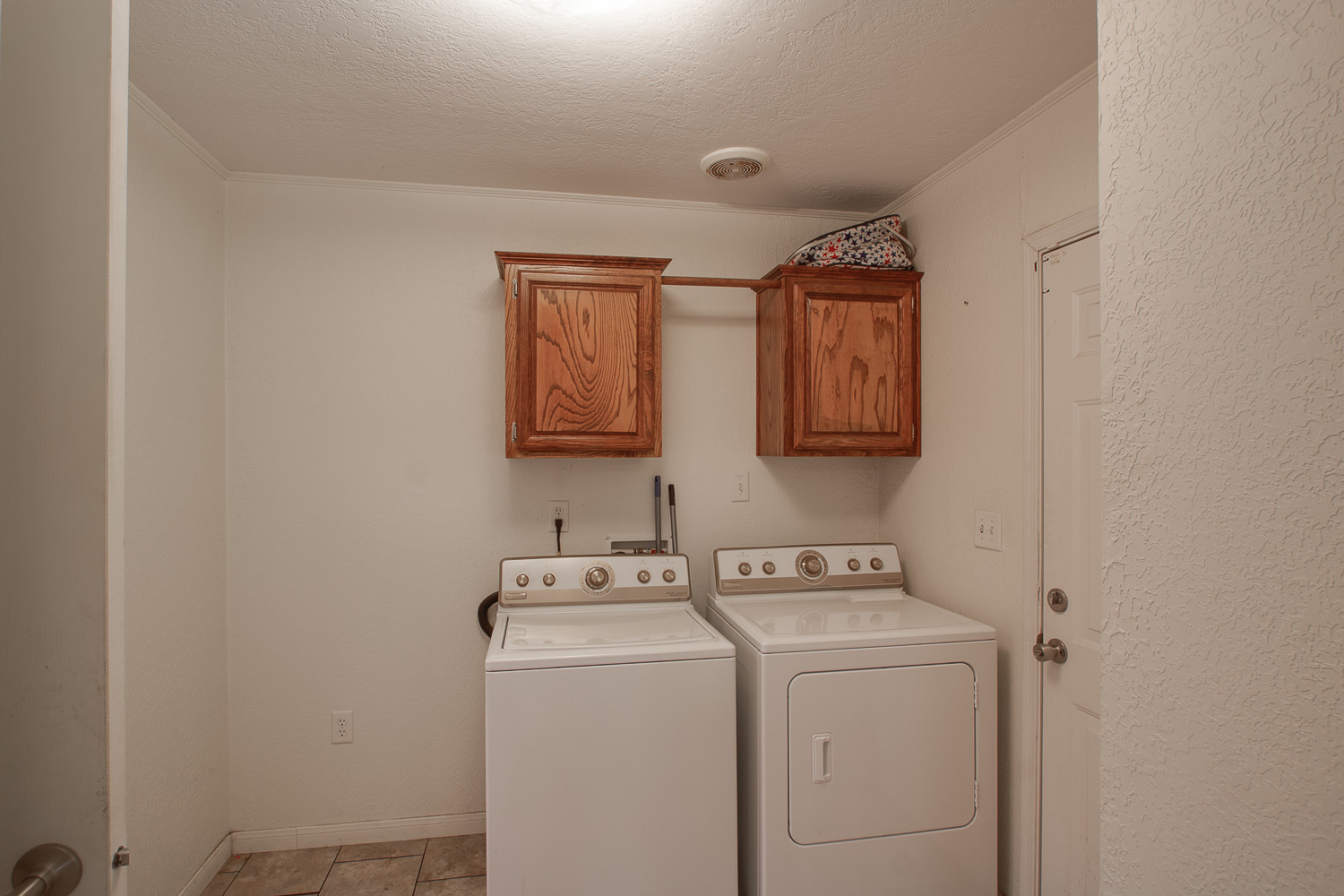 133 Mark Adams Road Del Valle, TX 78617 - Photo 17 of 20 An organized laundry space featuring overhead wood cabinetry and tile flooring.