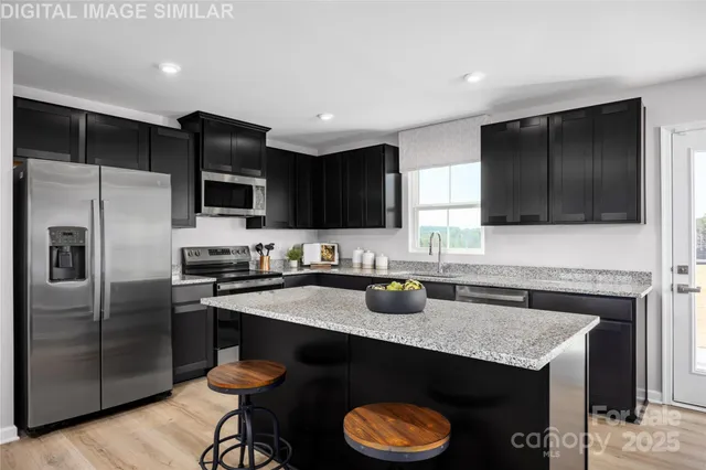 a kitchen with granite countertop stainless steel appliances a sink dishwasher a refrigerator a stove top oven and a center island with wooden floor