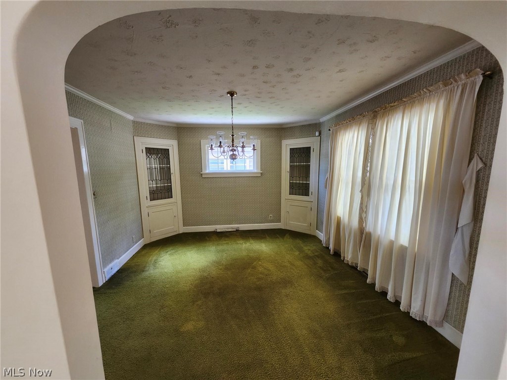Unfurnished dining area featuring a notable chandelier, dark colored carpet, a textured ceiling, and crown molding