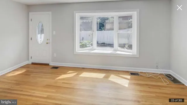 a view of an empty room with wooden floor and a window