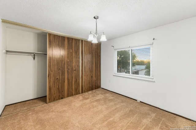 a view of an empty room with window and chandelier fan