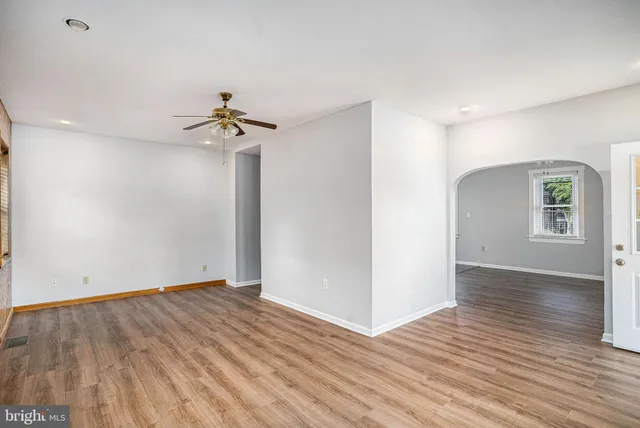an empty room with wooden floor ceiling fan and windows