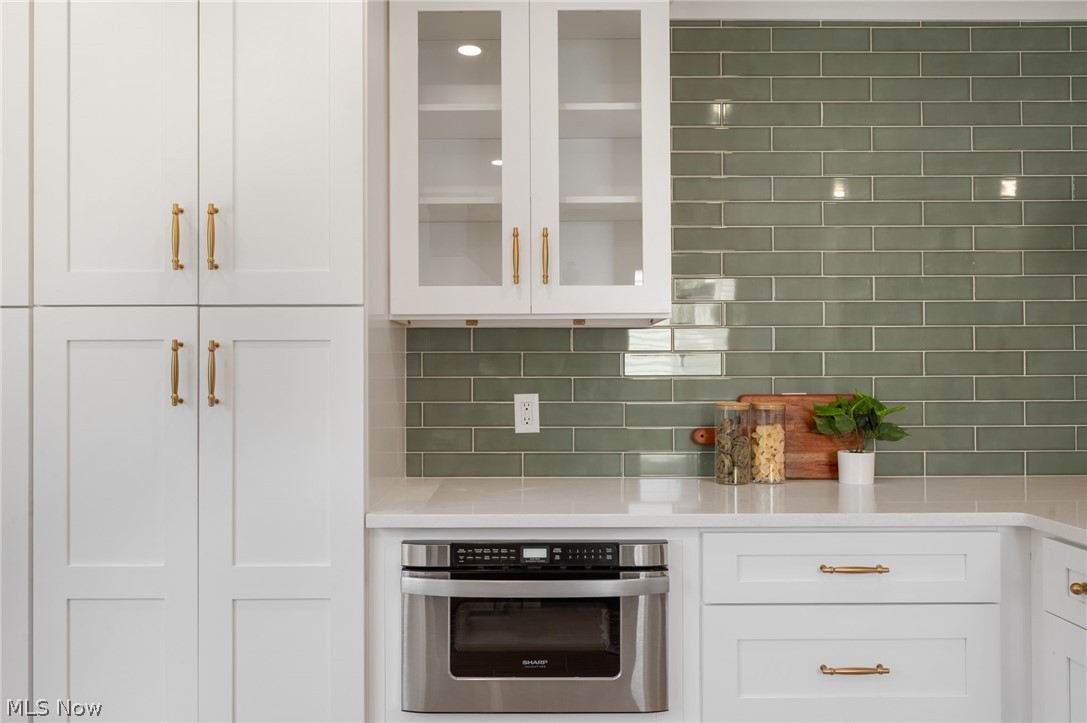 22625 Rye Road Shaker Heights, OH 44122 - Photo 12 of 38 White shaker-style cabinetry with gold-toned hardware, featuring glass-front upper cabinets and a built-in stainless steel microwave