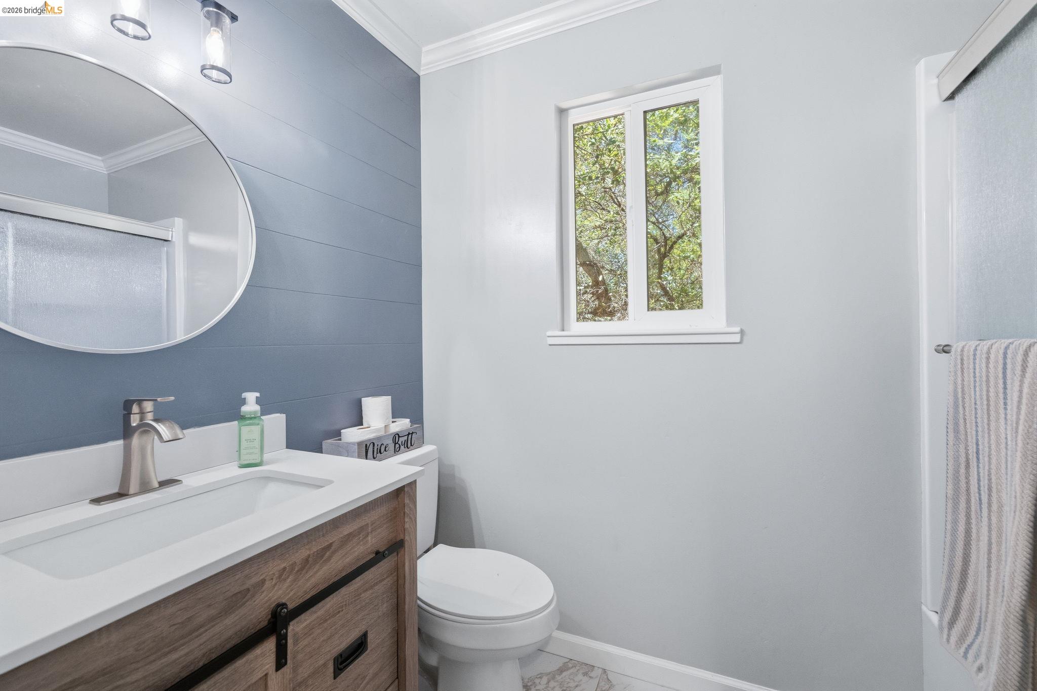 19059 Raboul Court Groveland, CA 95321 - Photo 15 of 21 Bathroom featuring a wood-finish vanity with a white countertop and integrated sink, brushed nickel faucet, round wall-mounted mirror, and a wall-mounted light fixture