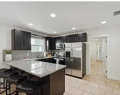 a kitchen with stainless steel appliances granite countertop a refrigerator a sink a stove a dining table and chairs