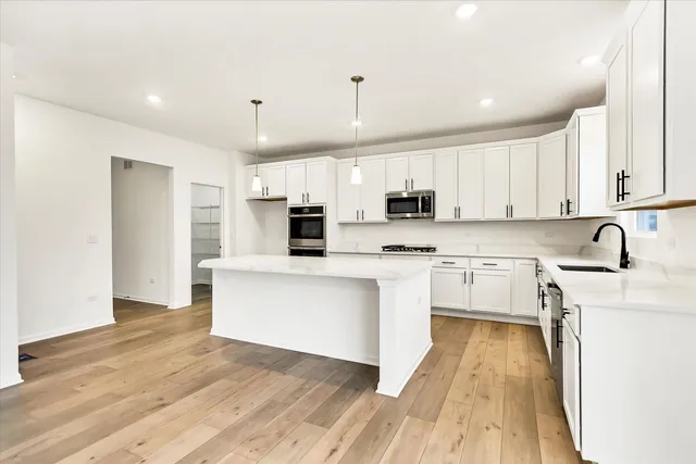 a kitchen with stainless steel appliances a microwave a stove a sink dishwasher a refrigerator and white cabinets with wooden floor