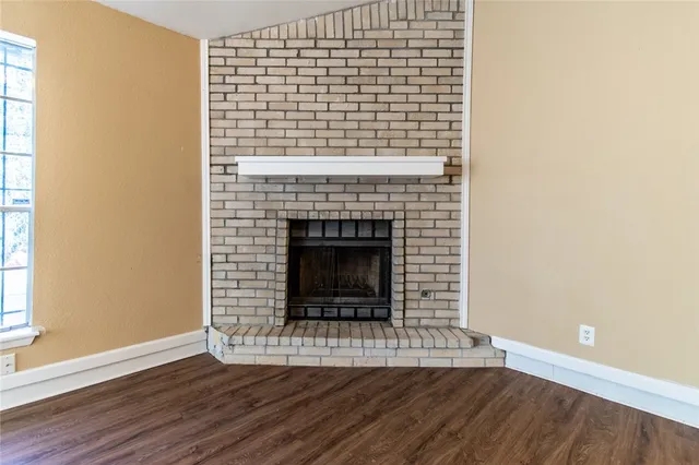 a view of an empty room with wooden floor a fireplace and a window