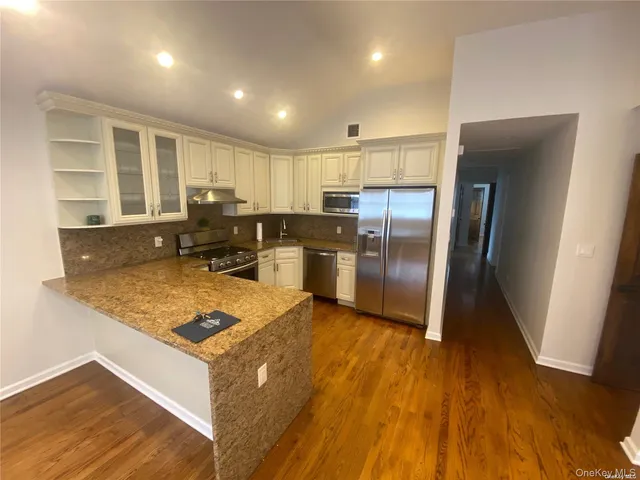 a kitchen with stainless steel appliances granite countertop a refrigerator oven a sink dishwasher and white cabinets with wooden floor