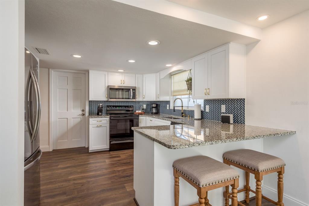 9110 Rainbow Lane Port Richey, FL 34668 - Photo 4 of 29 a kitchen with kitchen island granite countertop stainless steel appliances stove refrigerator dining table and chairs