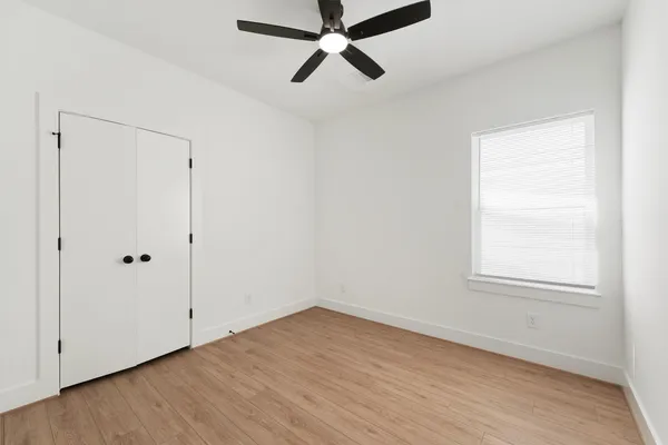 an empty room with wooden floor ceiling fan and windows