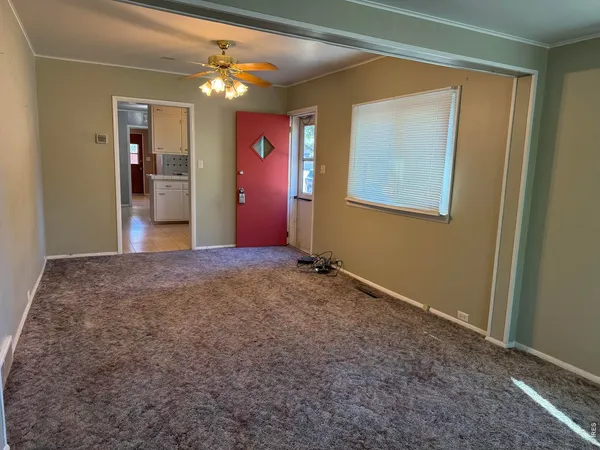 an empty room with a chandelier fan and windows