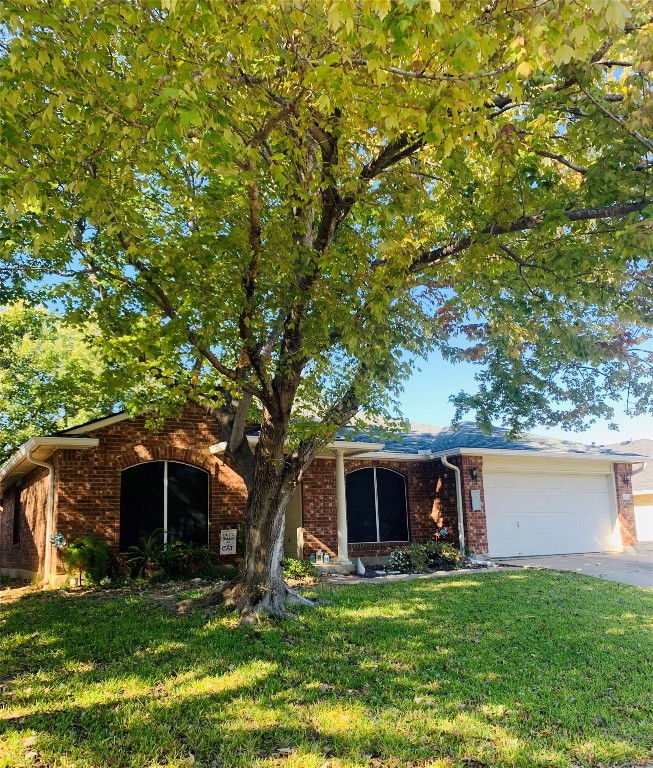 Ranch-style home featuring a front lawn, a garage, brick siding, and driveway